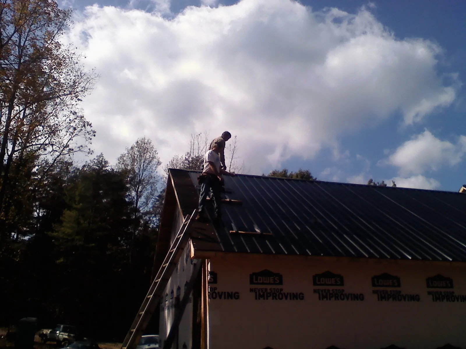 Roofer fastening dark metal panels high against a cloudy sky, from a Roof Inspection job in Dundas
