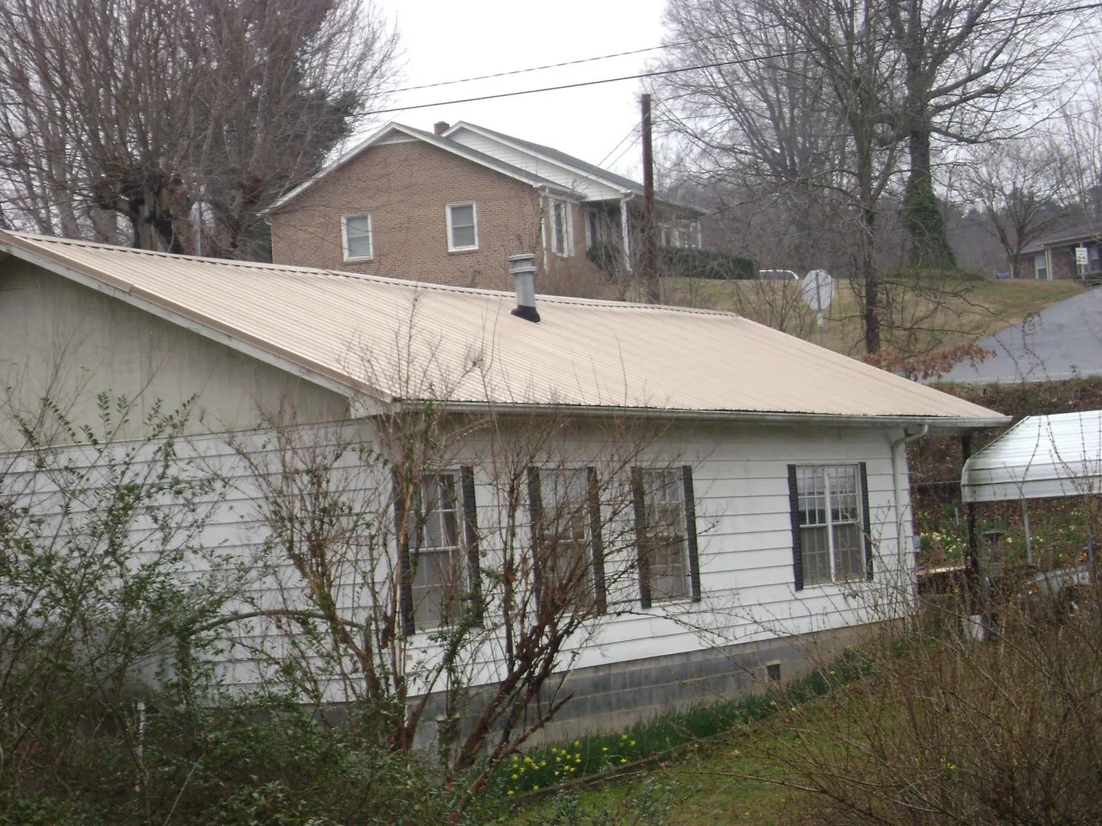 Tan metal roof on a white sided house set into a hillside — Commercial Roofing by Roofing Brothers in Dundas